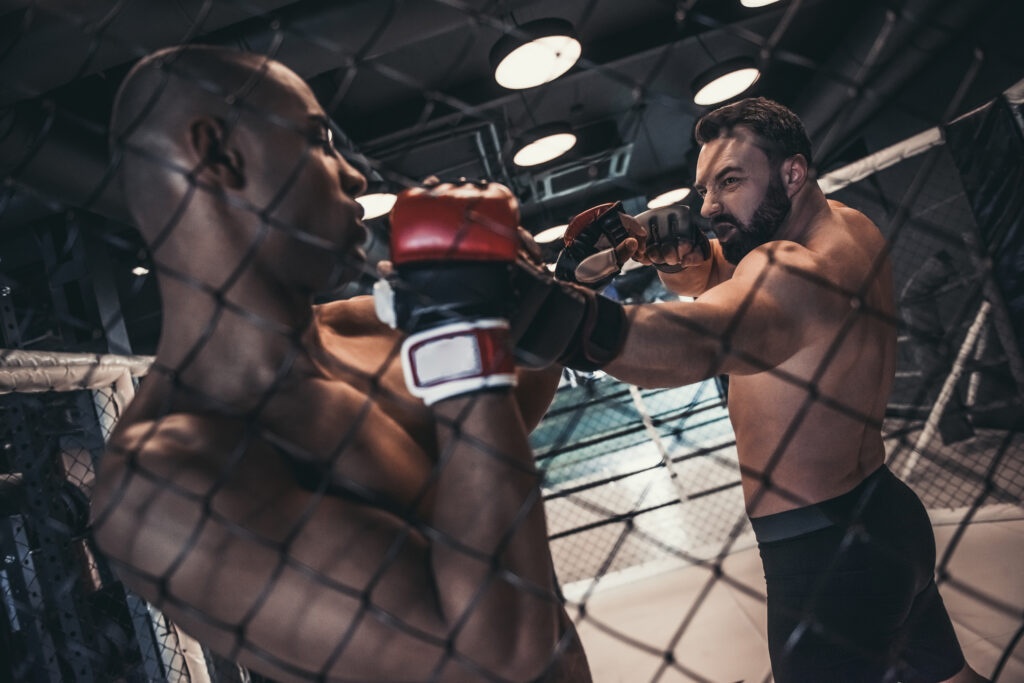 Two men in boxing gloves and shorts are fighting in cage
